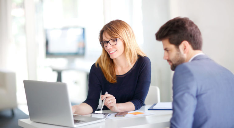 Portrait of investment advisor businesswoman sitting at office in front of computer and consulting with young professional man.